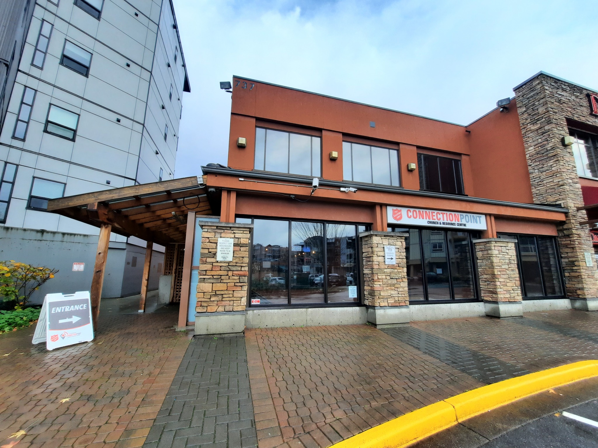 Exterior of The Salvation Army Connection Point Church and Resource Centre building, showing the entrance with glass doors, stone pillars, and Connection Point signage, with a covered walkway and brick pavement in front.